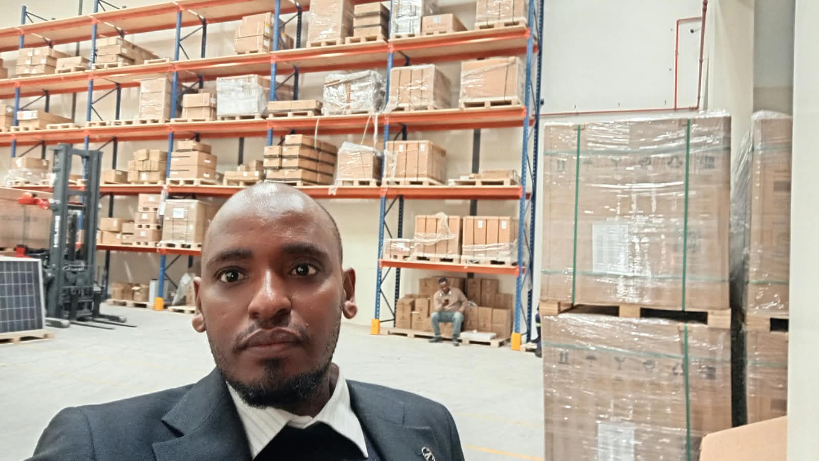 Techniqer Solutions Limited engineer inside stocked Kenyan solar equipment warehouse with pallets of panels, inverters, and batteries